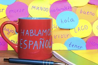 A coffee mug on a desk that says "Hablamos espanol".