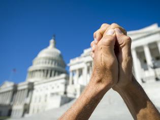 Two hands clasped together in front of a state capital building.