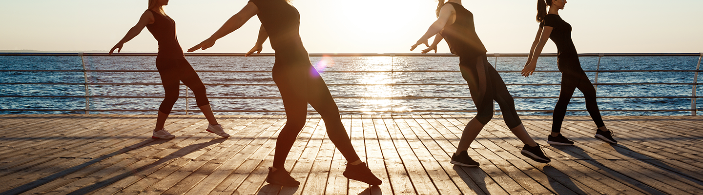 Silhouettes of sportive women dancing near sea at sunrise