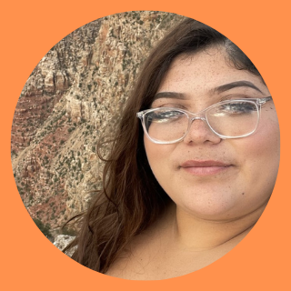 Female with glasses standing in front of mountain.