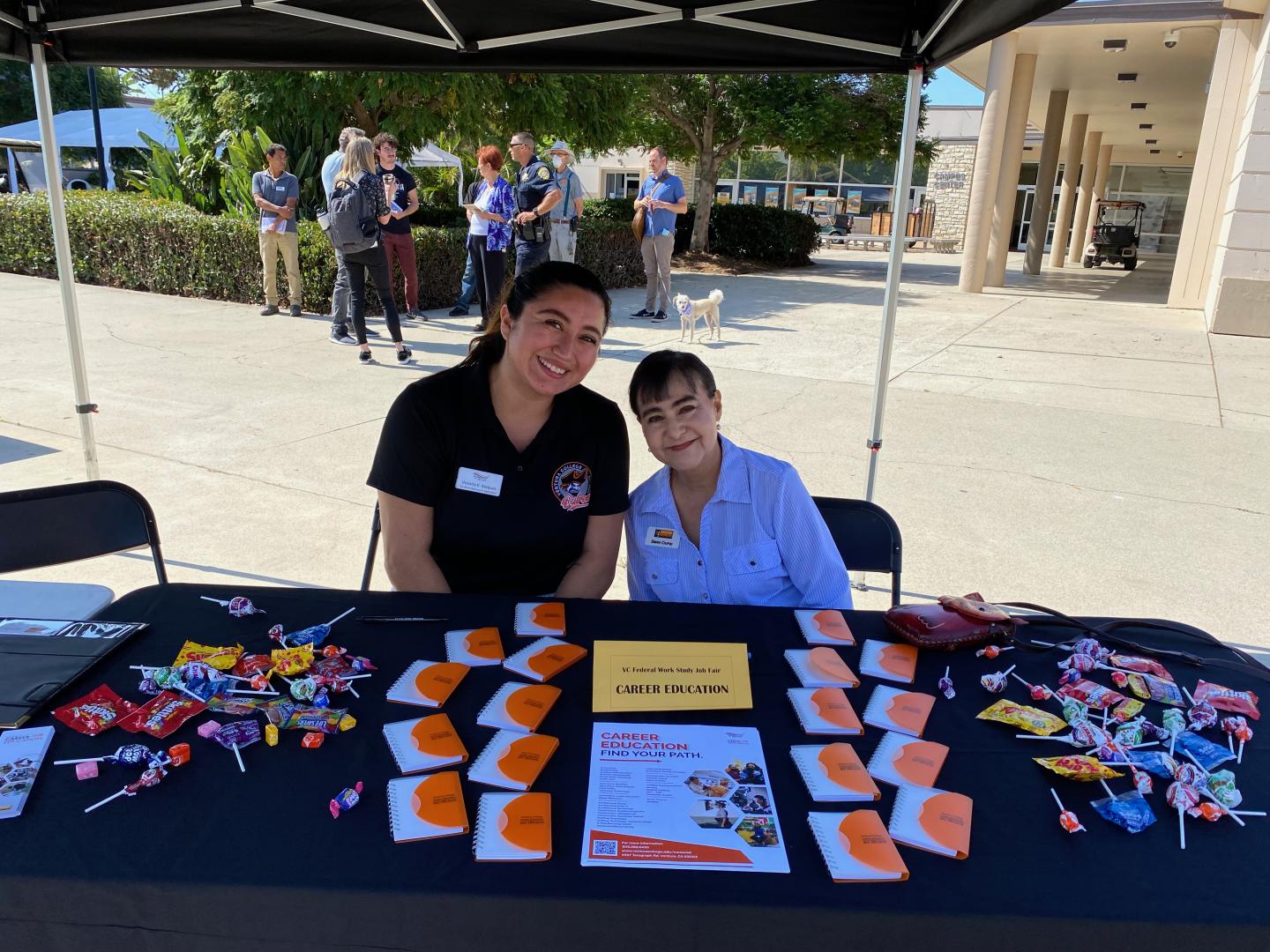 Career Education Table at Job Fair.  Two Classified Professionals sitting and smiling at table.