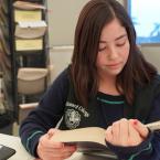 Young student wearing Oxnard College vest reading textbook i