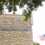 Sign on the side of a building that reads "Veterans Resource Center" with the American flag flying in the background.