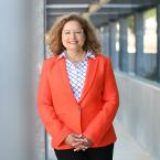 President Lourido-Habib leaning against a column, wearing a VC Orange blazer, black pants, and print blouse