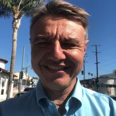 Alex smiling outside under a palm tree