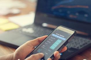 A person comparing financial stocks on a smart phone and a laptop.