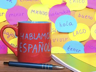 A coffee mug on a desk that says "Hablamos espanol".