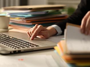 A person sitting in front of a computer and a stack of documents.