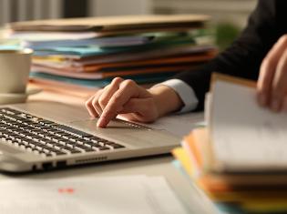 A person sitting in front of a computer and a stack of documents.