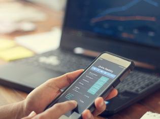 A person comparing financial stocks on a smart phone and a laptop.