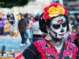 A person wearing day of the dead sugar skull make-up, a flower headband, and traditional spanish dress.