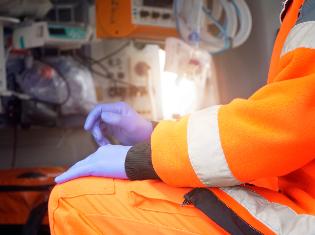 An emergency medical person in full garb, sitting inside an ambulance.