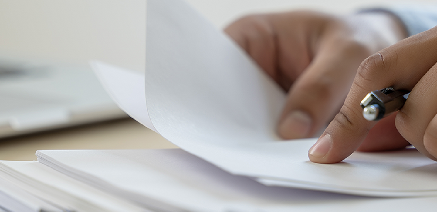 A person going through documents on a desk with a pen in hand.