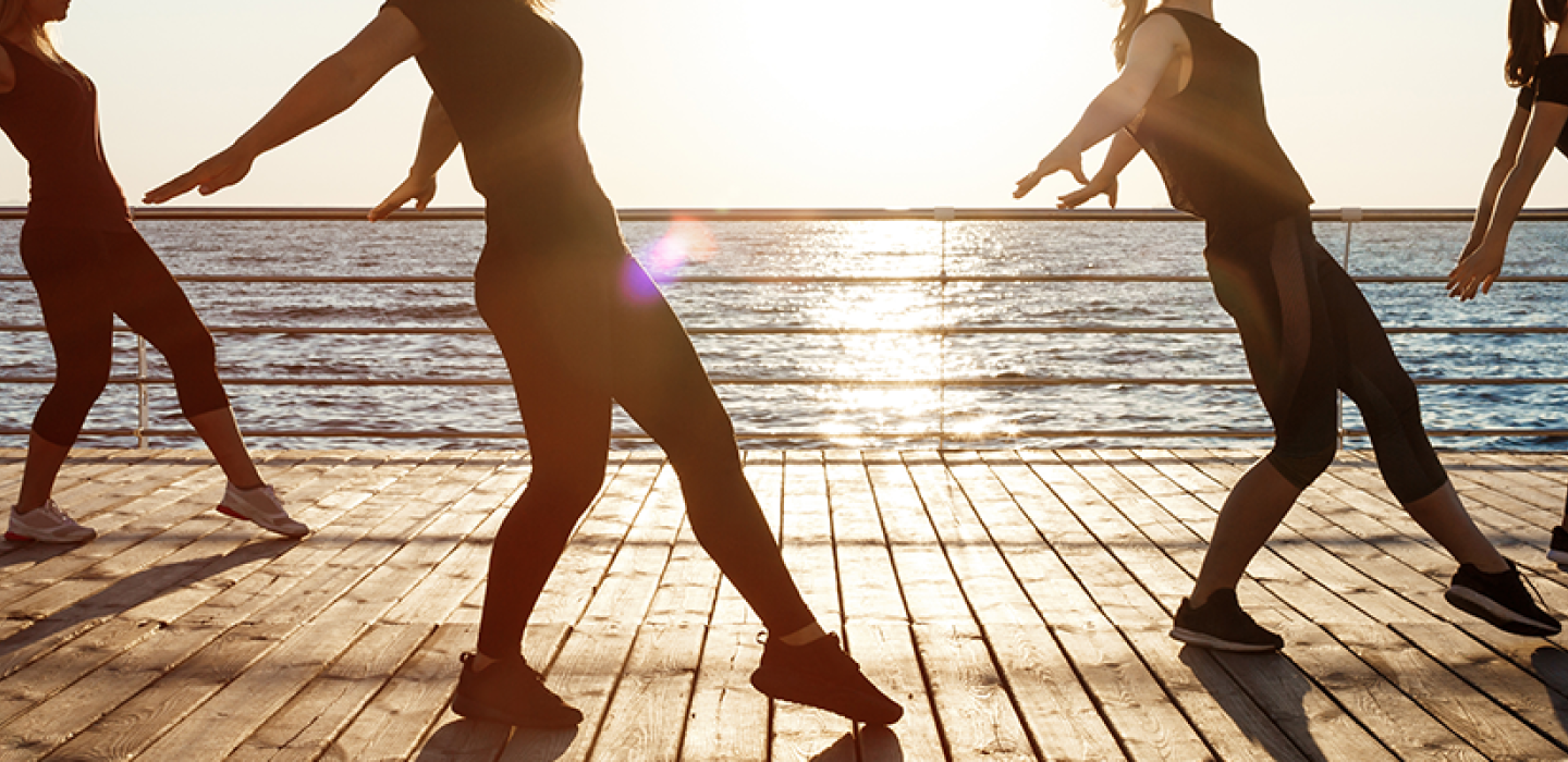 Silhouettes of sportive women dancing near sea at sunrise