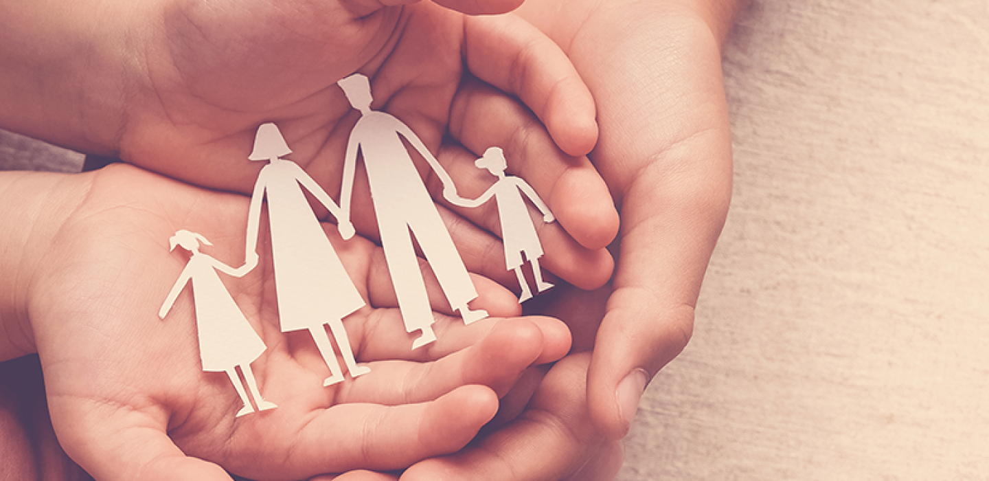 Several hands holding a paper cut out of a family.