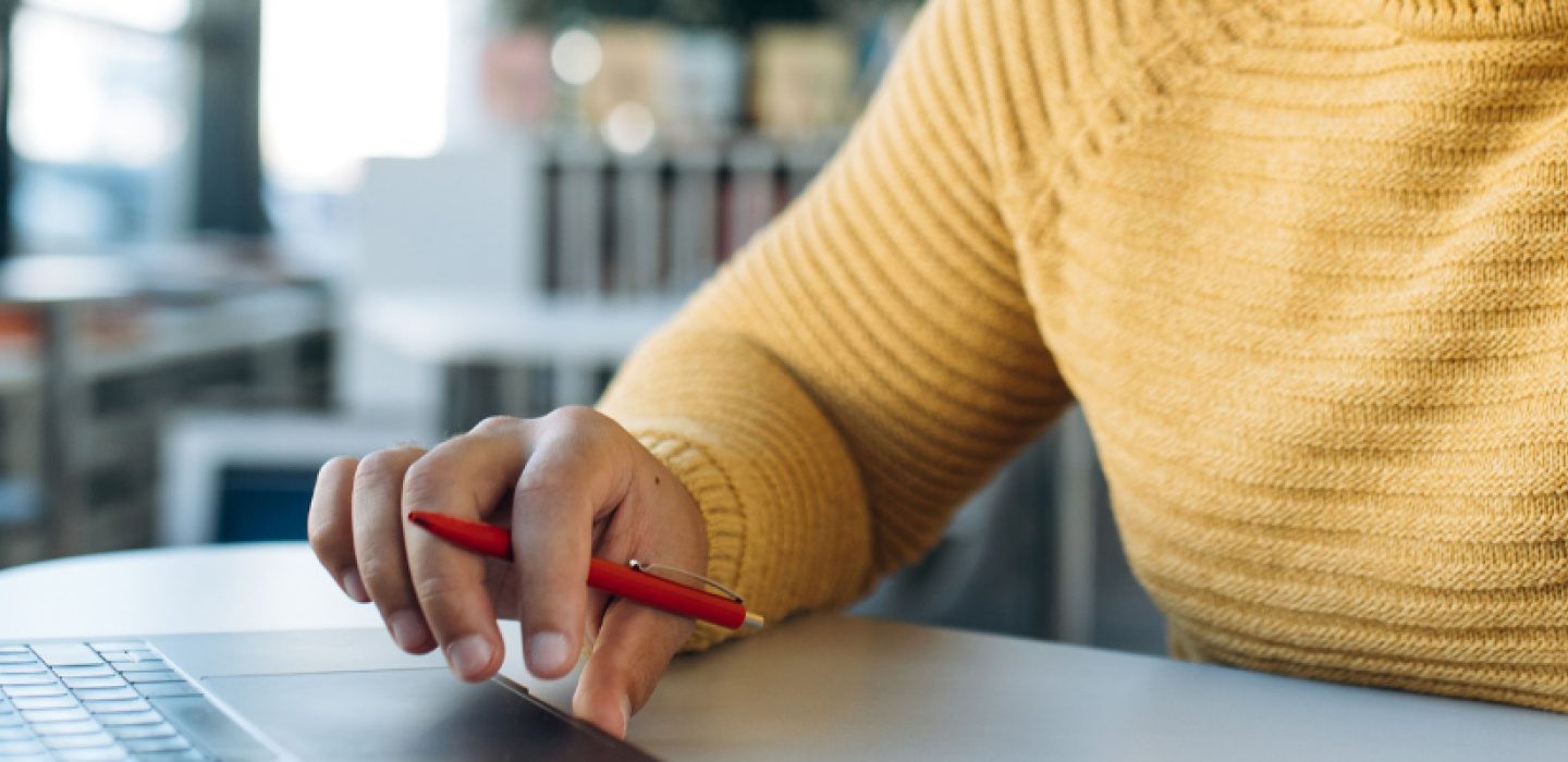 Hand holding pen while working at a laptop