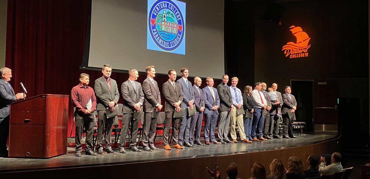 Students stand on stage for Paramedic Studies Program graduation. 