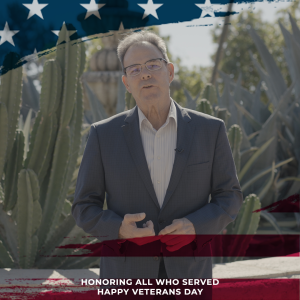 A man in a suit stands among cacti with a fountain in the ba