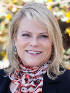 Kim Hoffmans, woman with blond hair smiling and wearing a red and white scarf