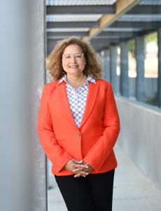 President Lourido-Habib leaning against a column, wearing a VC Orange blazer, black pants, and print blouse